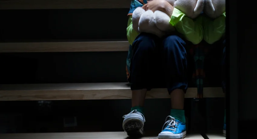 Un petit garçon effrayé assis dans les escaliers la nuit avec son nounours